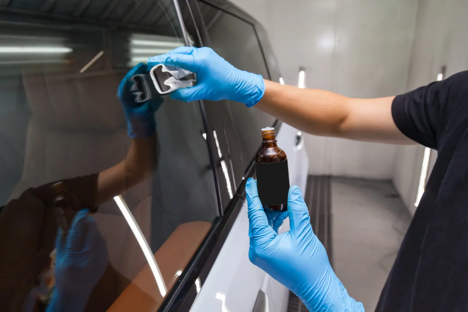 Person in blue gloves applying liquid to a car window using an applicator.